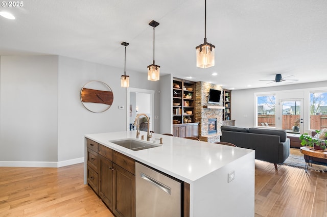 kitchen featuring dishwasher, a kitchen island with sink, sink, ceiling fan, and a fireplace