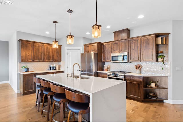 kitchen featuring a kitchen island with sink, hanging light fixtures, sink, light hardwood / wood-style flooring, and stainless steel appliances