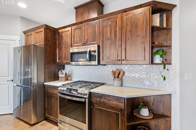 kitchen with light wood-type flooring, appliances with stainless steel finishes, and backsplash