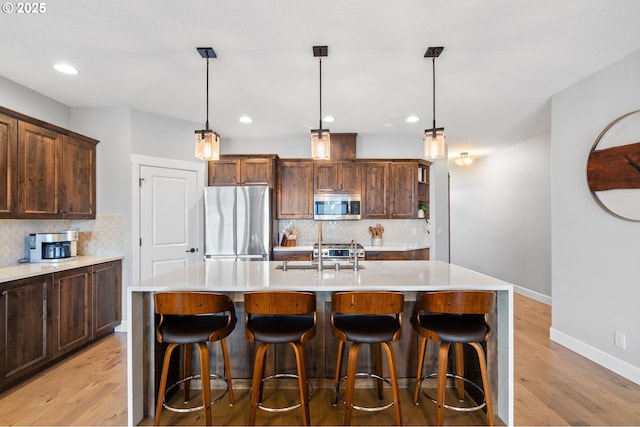 kitchen featuring appliances with stainless steel finishes, backsplash, a center island with sink, and pendant lighting