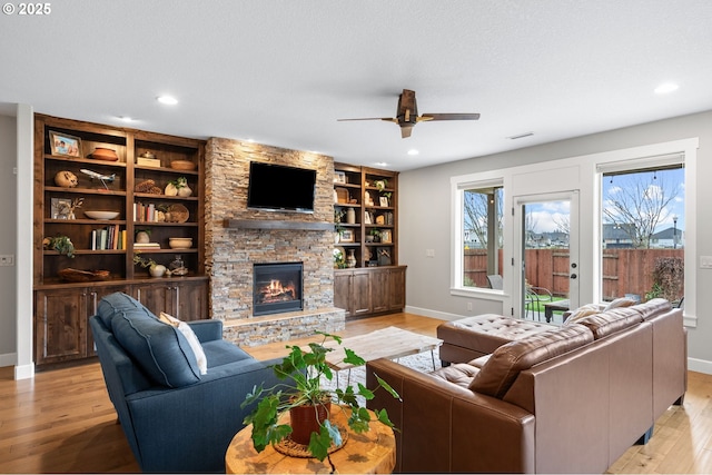 living room featuring a stone fireplace, ceiling fan, built in features, and light wood-type flooring