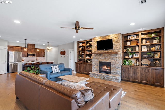 living room featuring ceiling fan, light wood-type flooring, a fireplace, and built in shelves