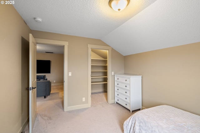 bedroom featuring light carpet, vaulted ceiling, a spacious closet, a textured ceiling, and a closet