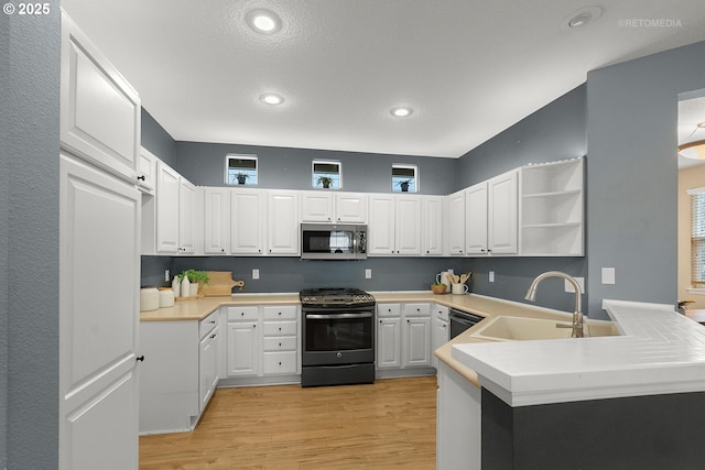 kitchen featuring a sink, light wood-style flooring, a peninsula, stainless steel appliances, and open shelves