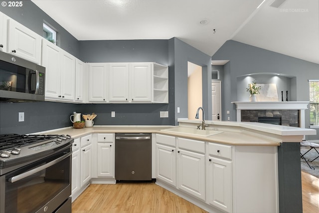 kitchen featuring a tiled fireplace, a sink, stainless steel appliances, a peninsula, and light wood finished floors