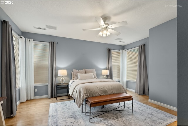 bedroom featuring light wood-type flooring, baseboards, a textured ceiling, and visible vents