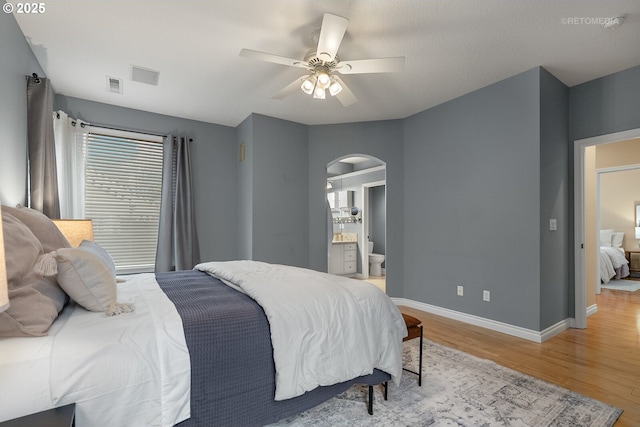 bedroom with a ceiling fan, visible vents, light wood finished floors, baseboards, and arched walkways