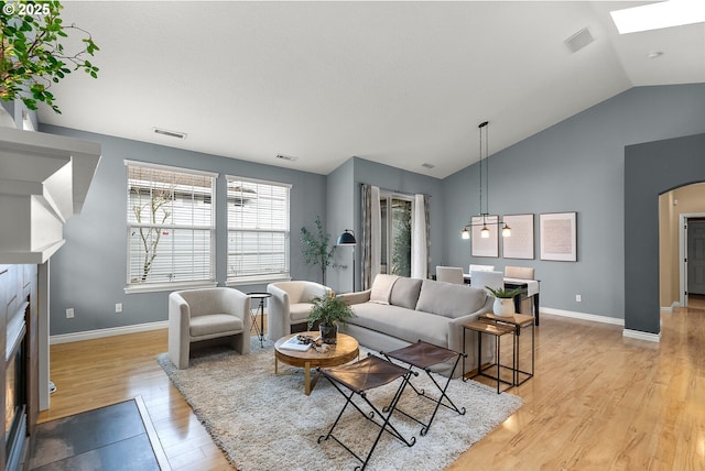 living room with light wood finished floors, visible vents, arched walkways, and vaulted ceiling