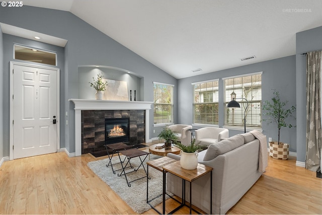 living room featuring vaulted ceiling, visible vents, a tile fireplace, and wood finished floors