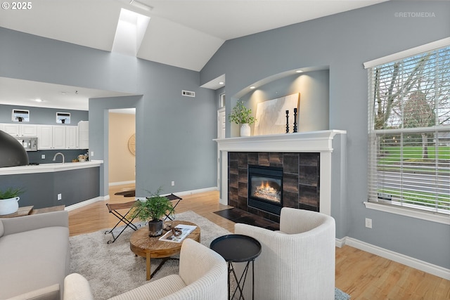 living area featuring light wood finished floors, baseboards, a wealth of natural light, and a tile fireplace