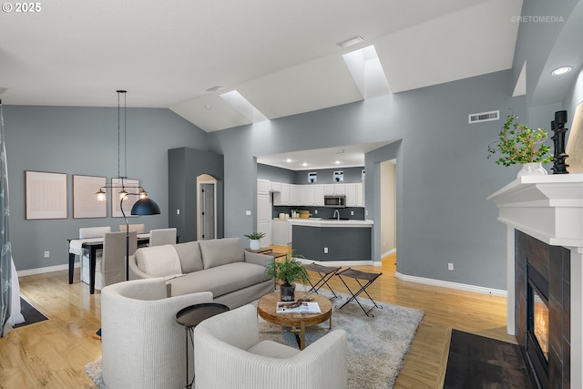 living area with visible vents, a fireplace with flush hearth, light wood-style floors, baseboards, and vaulted ceiling