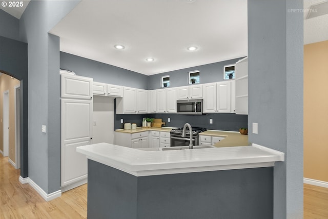 kitchen featuring light wood-type flooring, appliances with stainless steel finishes, a peninsula, arched walkways, and white cabinets