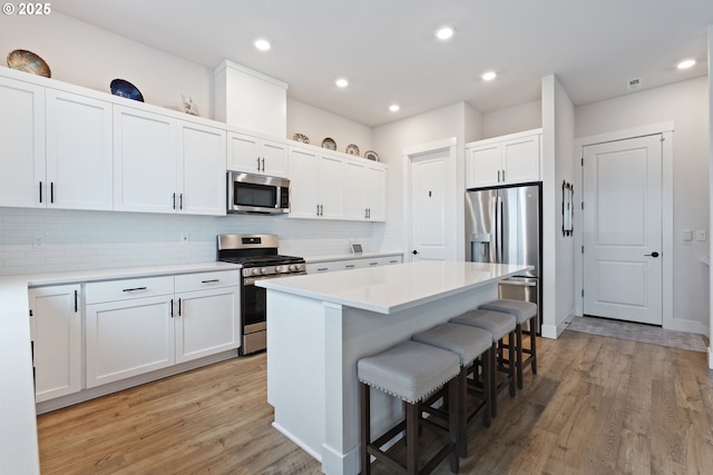 kitchen with a kitchen bar, stainless steel appliances, a kitchen island, light hardwood / wood-style flooring, and white cabinetry