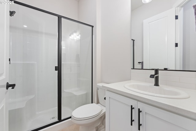 bathroom with vanity, toilet, a shower with shower door, and backsplash