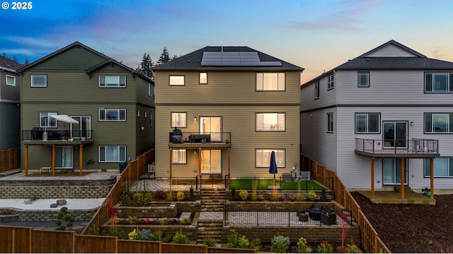 back house at dusk featuring solar panels, a balcony, and a patio area