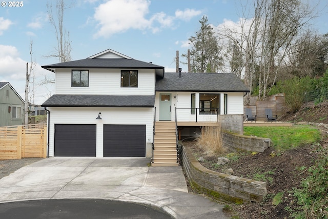 split level home with a shingled roof, concrete driveway, fence, a garage, and stairs