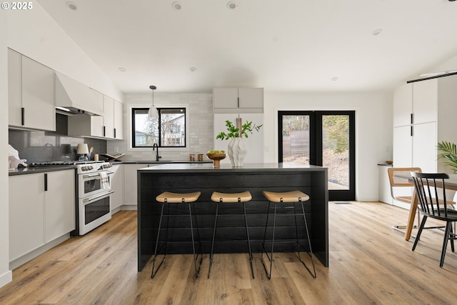 kitchen with white cabinetry, light wood-style floors, double oven range, tasteful backsplash, and dark countertops