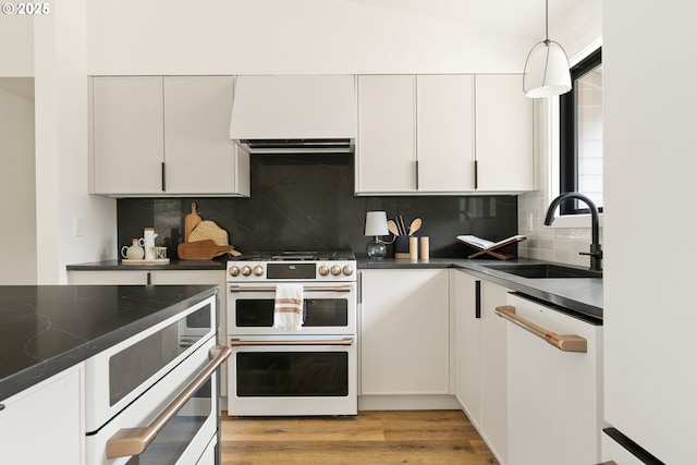 kitchen featuring light wood-style flooring, white appliances, a sink, backsplash, and dark countertops