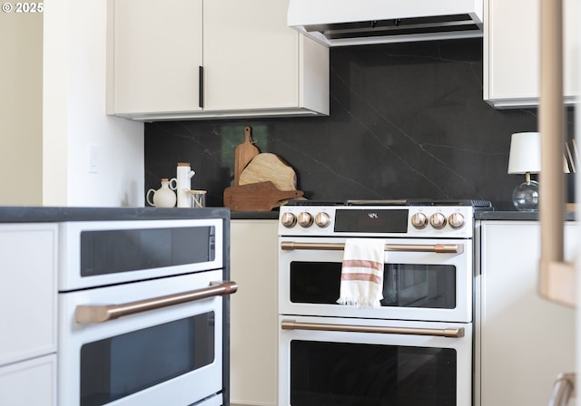 kitchen featuring dark countertops, double oven range, white cabinetry, backsplash, and exhaust hood