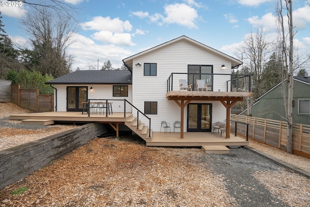 rear view of house with a balcony, a fenced backyard, a wooden deck, and french doors