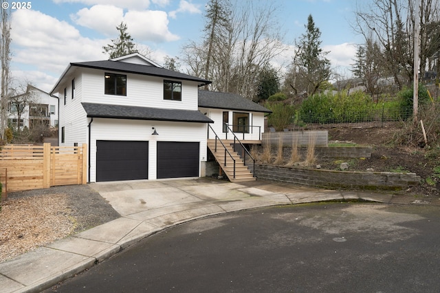 split level home featuring roof with shingles, stairway, an attached garage, fence, and driveway