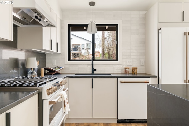 kitchen featuring white appliances, dark countertops, backsplash, wall chimney range hood, and a sink