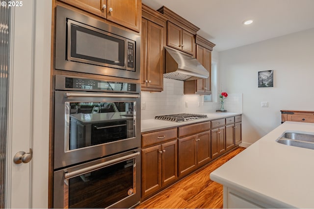 kitchen featuring under cabinet range hood, light countertops, decorative backsplash, light wood-style flooring, and stainless steel appliances