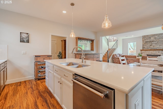 kitchen with dishwasher, wood finished floors, hanging light fixtures, white cabinetry, and a sink