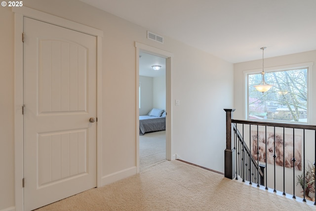 hall with visible vents, an upstairs landing, baseboards, and carpet flooring