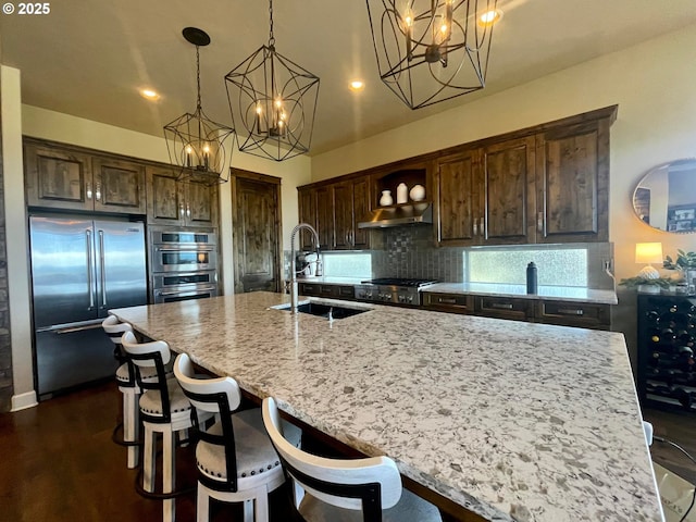 kitchen with decorative light fixtures, stainless steel appliances, an island with sink, decorative backsplash, and sink