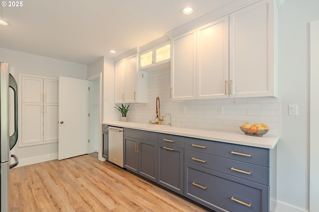 kitchen with white cabinetry, tasteful backsplash, a sink, light wood-style flooring, and appliances with stainless steel finishes