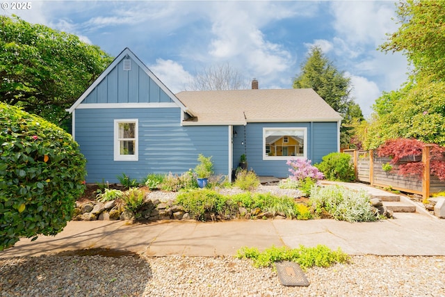 view of front of house featuring board and batten siding, fence, a chimney, and a shingled roof