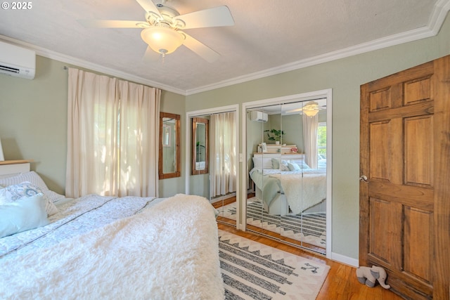 bedroom with an AC wall unit, crown molding, multiple closets, and light wood finished floors