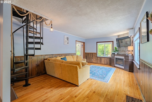 living area featuring wooden walls, a textured ceiling, light wood-type flooring, and a wainscoted wall