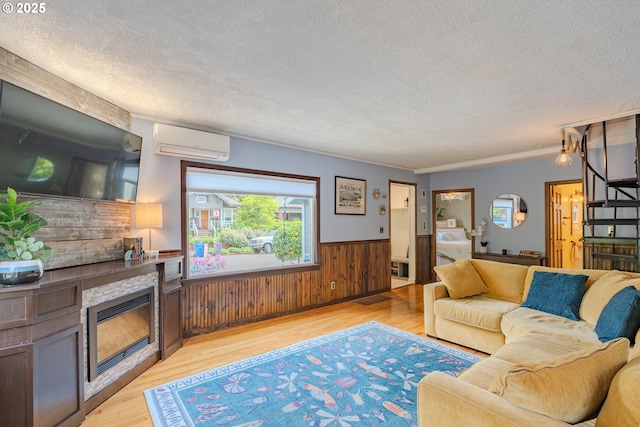 living room featuring a glass covered fireplace, light wood-style floors, an AC wall unit, a textured ceiling, and a wainscoted wall