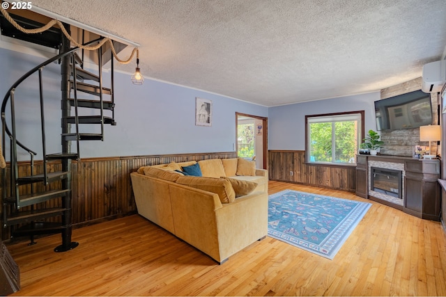 living area with a textured ceiling, a wall mounted AC, a wainscoted wall, light wood finished floors, and stairs