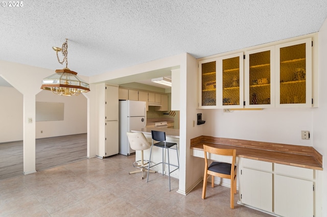 kitchen with light tile patterned floors, white cabinetry, white refrigerator, a textured ceiling, and decorative light fixtures