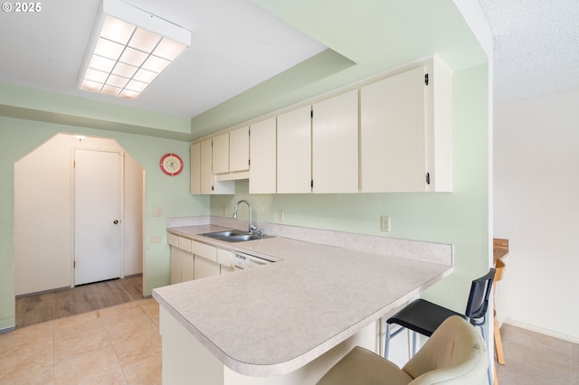 kitchen featuring sink, light tile patterned floors, a kitchen breakfast bar, white cabinets, and kitchen peninsula