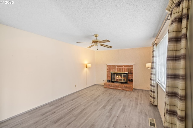 unfurnished living room featuring ceiling fan, a fireplace, light hardwood / wood-style floors, and a textured ceiling