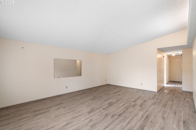 empty room with lofted ceiling, light hardwood / wood-style flooring, and a textured ceiling