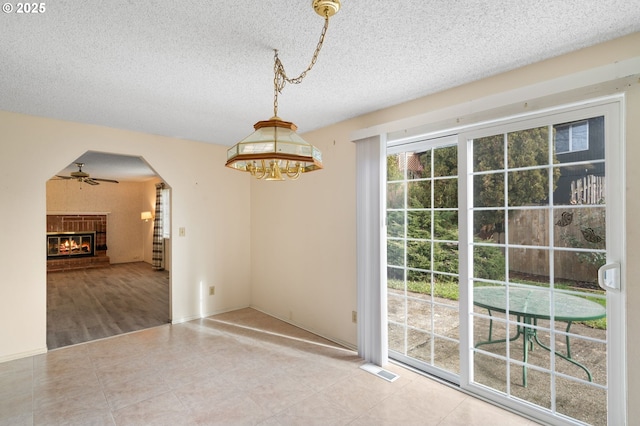 unfurnished dining area with tile patterned flooring, a brick fireplace, a textured ceiling, and ceiling fan