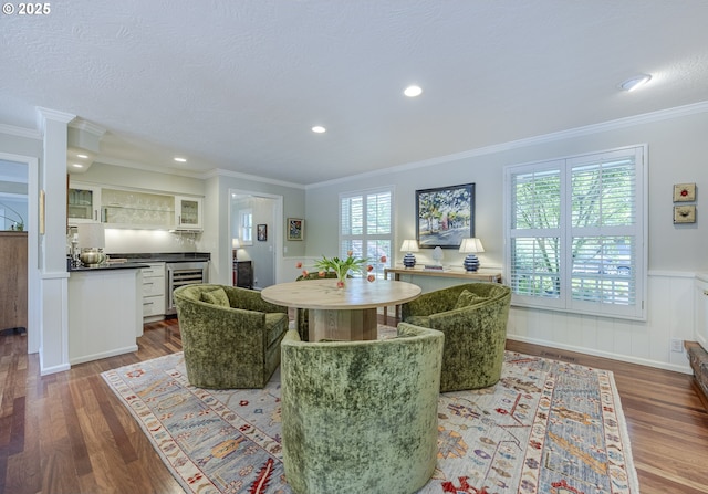 dining area featuring bar area, wood finished floors, wine cooler, a wainscoted wall, and ornamental molding