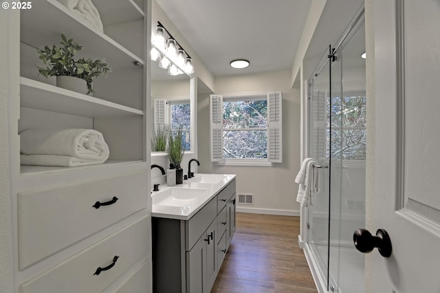 full bathroom featuring double vanity, a stall shower, visible vents, wood finished floors, and a sink