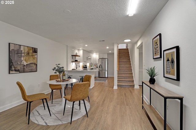 dining area with recessed lighting, light wood-style floors, a textured ceiling, baseboards, and stairs