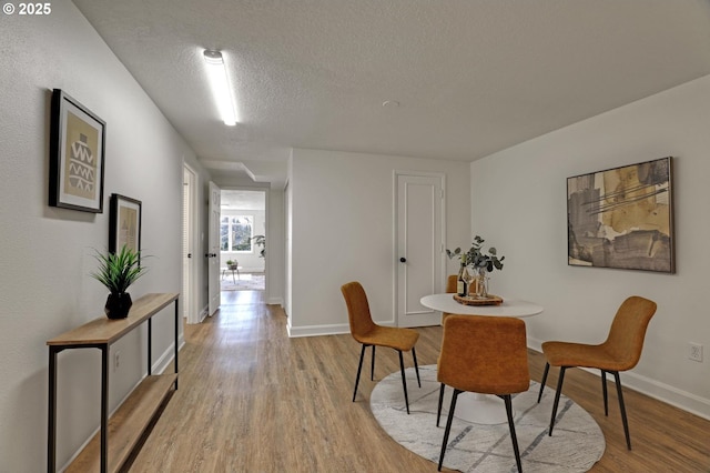 dining area featuring light wood-style floors, a textured ceiling, and baseboards