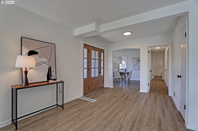 foyer entrance with visible vents, a textured ceiling, baseboards, and wood finished floors