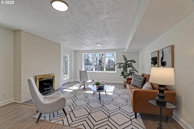 living area featuring a fireplace, a textured ceiling, baseboards, and wood finished floors