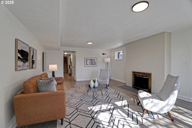 living room with a brick fireplace, a textured ceiling, baseboards, and wood finished floors