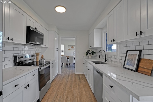 kitchen featuring a sink, white cabinets, appliances with stainless steel finishes, light wood-type flooring, and tasteful backsplash