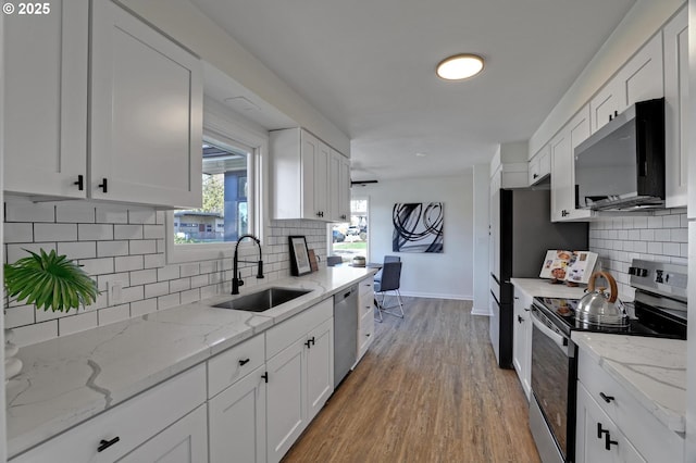 kitchen with light wood finished floors, stainless steel appliances, white cabinets, a sink, and baseboards